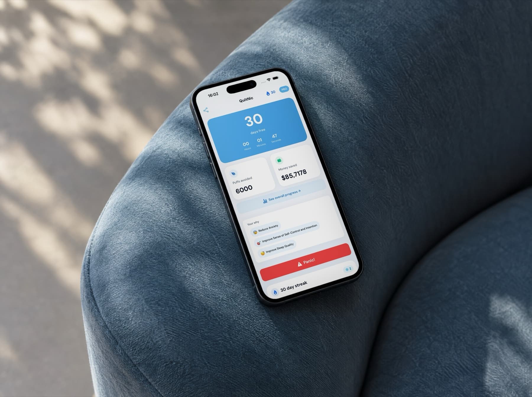 En iPhone på armlenet til en blå lenestol i morgenlys. Skjermen viser QuitNic-appens dashbord: 30 dager nikotinfri, med unngåtte puff og sparte penger.
